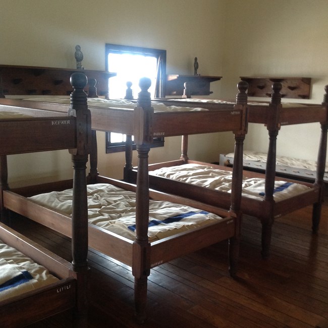 Wooden bunk beds lined up against the barrack walls with simple bedding
