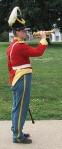 A uniformed bugler plays his horn on the parade grounds at Fort Scott