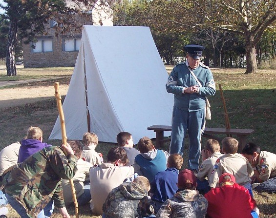 An interpreter in 1840s US infantry soldier dress addresses a group of children outside of a tent