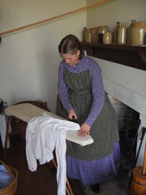 A laundress uses a flat iron to straighten out a shirt inside the barracks at Fort Scott