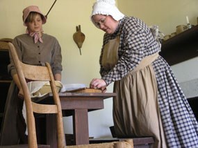 Two laundresses mend fabric on a table inside a historic structure at Fort Scott