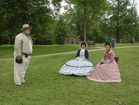 two women dressed in Civil War era dresses talk to a man dressed as a Confederate soldier