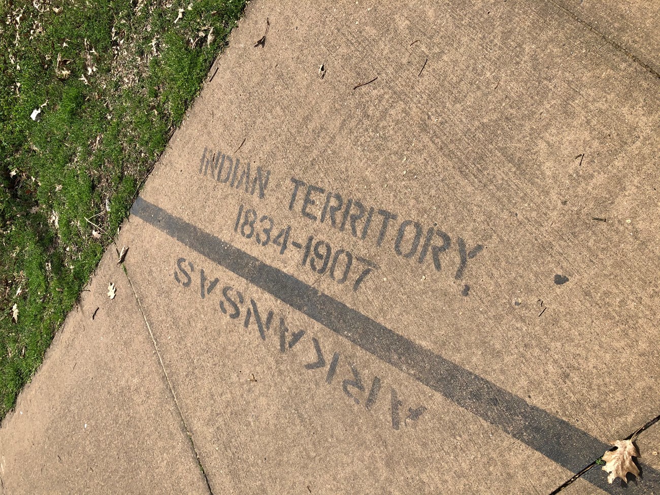 Black line painted across sidewalk with text on the right reading Indian Territory 1834-1907 and Arkansas on the left side of the line.