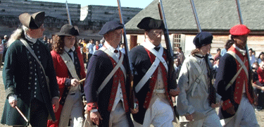 several men with stand in a straight row. white X's are formed on their fronts by uniform straps; they hold muskets