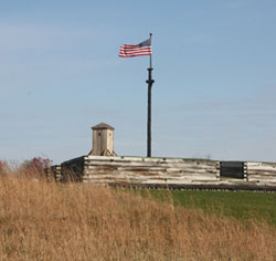 on a sunny fall afternoon, an American flag flutters in the wind over a brown hued wall. the sun makes the green grass and the flag's colors POP