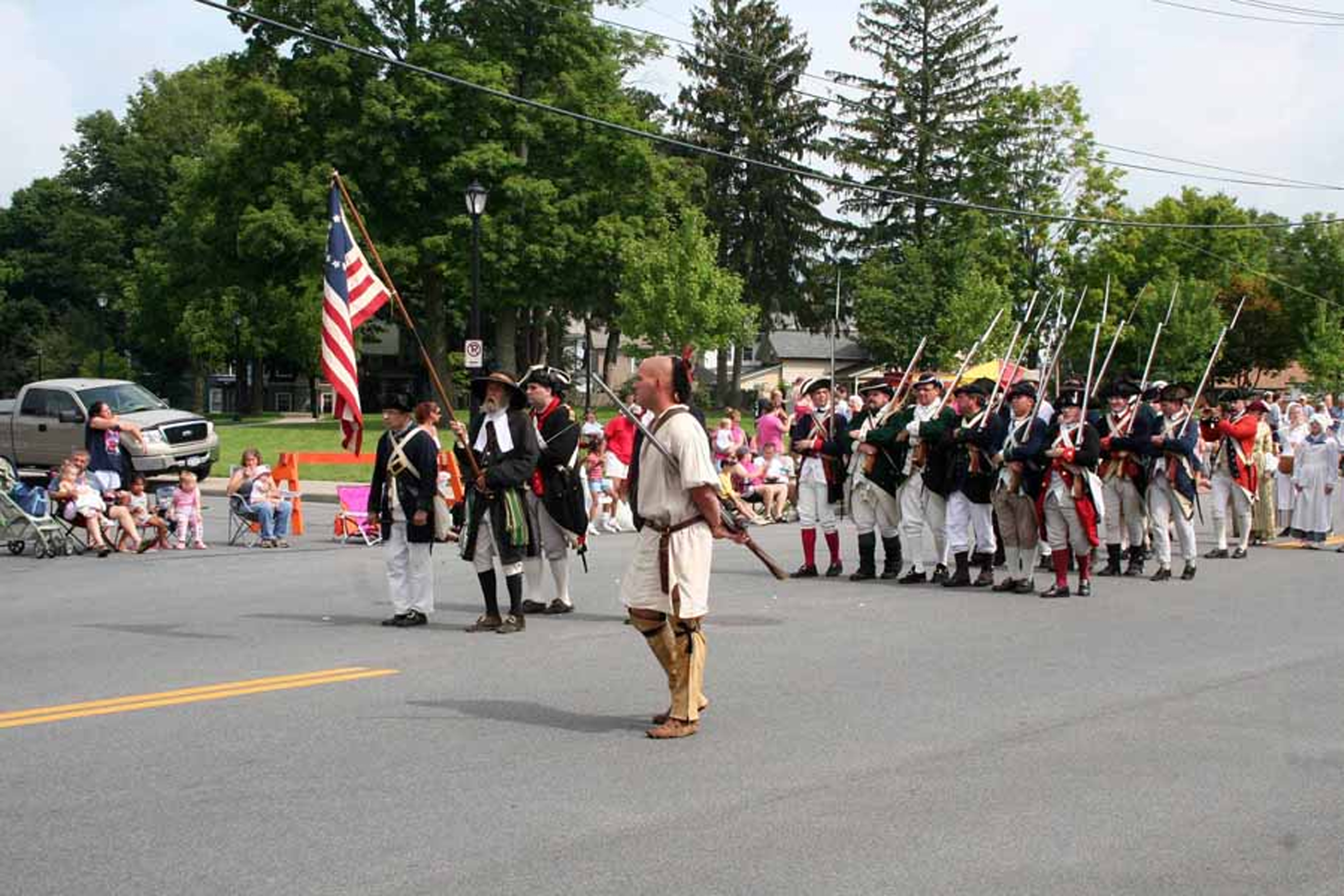 in a parade march, folks in period dress walk down a nicely decorated, and crowded city street
