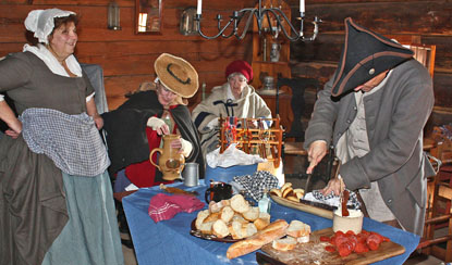 people in colorful 18th century clothing gather around a table with many different holiday items on it.