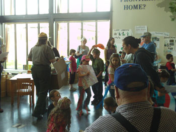 a busy foyer with children rushing about. they carry papers of many colors. A park ranger directs them