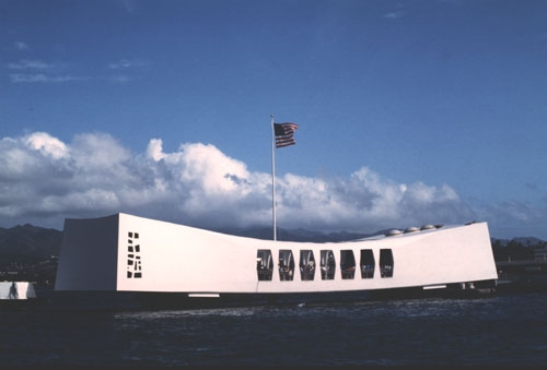 a curved large white box with windows sits on top of the ocean. a US flag flys above.
