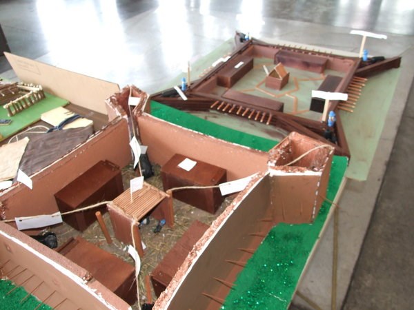 a sturdy brown cardboard model of forts with a green backing sits on a table. string ties crucial pieces together and labels them