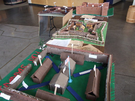 carefully constructed models of forts in brown cardboard and wood sit on tables with little white labels attached to different pieces