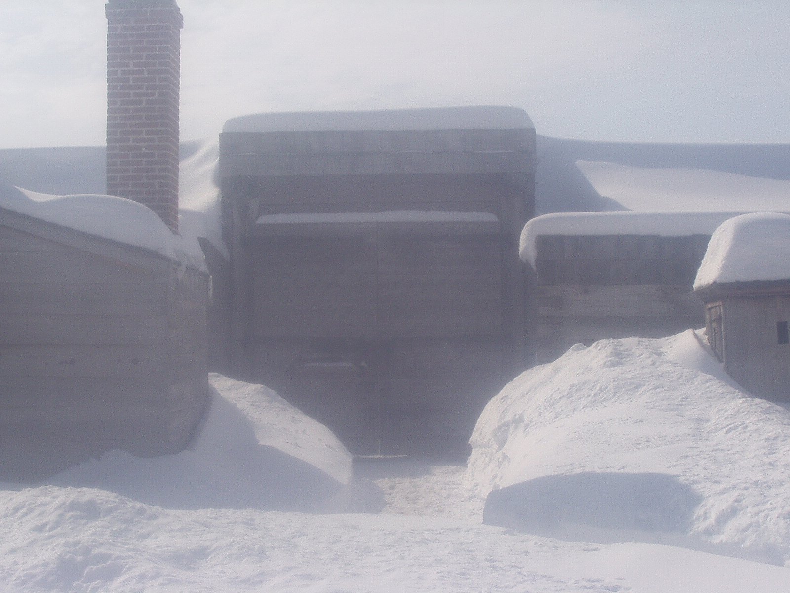 Fort Stanwix in winter, a white wall with a small brown gate pops through the snow. 