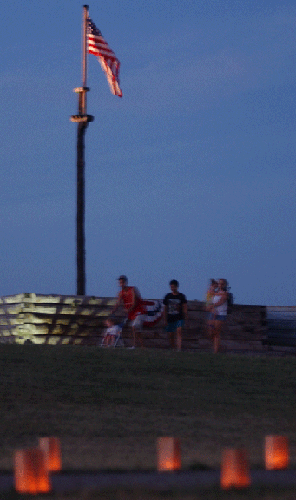 groups of people walk, bathed in orange candle light; a grey trail leads them forward