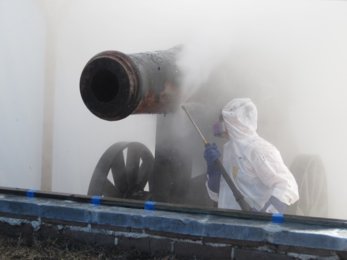 A conservator wears protective gear while spraying a cannon.