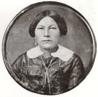 American Indian woman with hair pulled back wearing a dark dress with a white collar.