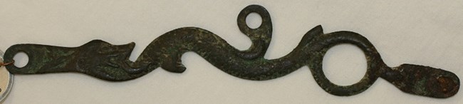 A green discolored metal piece in the design of a serpent.