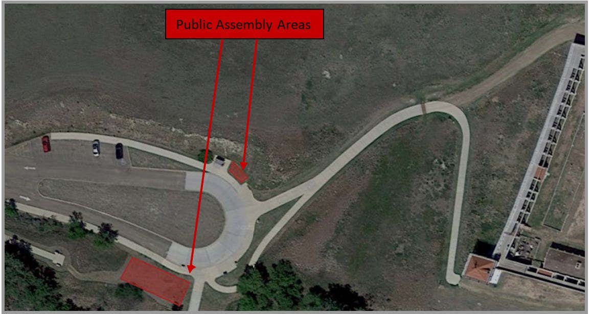 Aerial photo of a horseshoe shaped parking area on the left with a trail curving towards a set of buildings to right. Two red-shaded rectangles on outside of closed-end of horseshoe parking at 1 and 7 o'clock positions. Text reads Public Assembly Areas.
