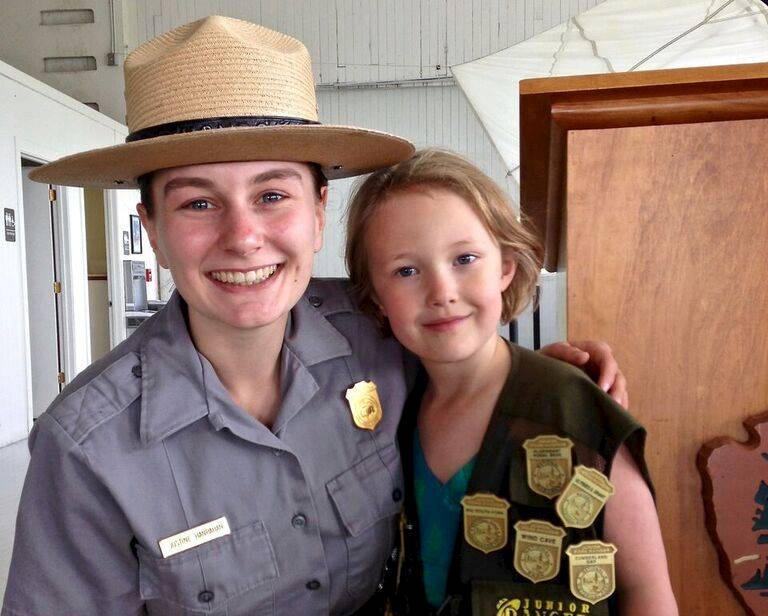 National Park Ranger posing with Junior Ranger wearing badges from many parks