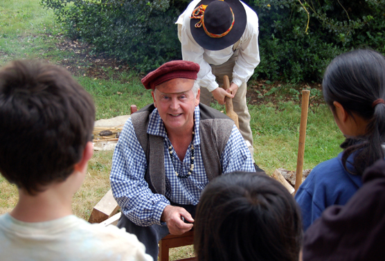 Park Guide Marv Binegar demonstrates woodcutting to three children at the annual Brigade Encampment special event.