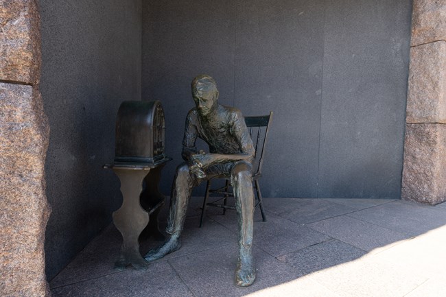 A bronze statue of a man sitting in a chair leaning toward a radio. The statue is under an aclove.