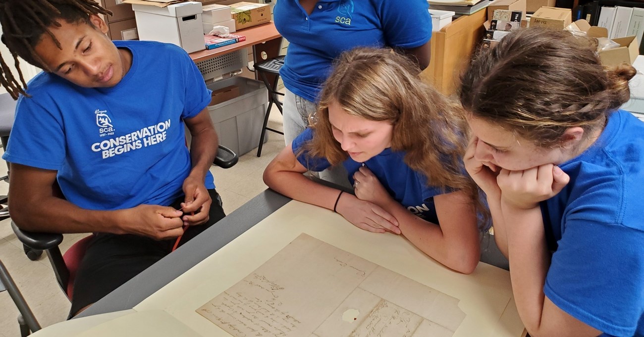 Three students in blue shirts looking at piece of paper on table