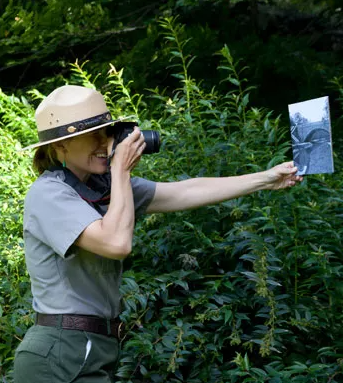 Park ranger in uniform and hat holds image up and takes picture of it