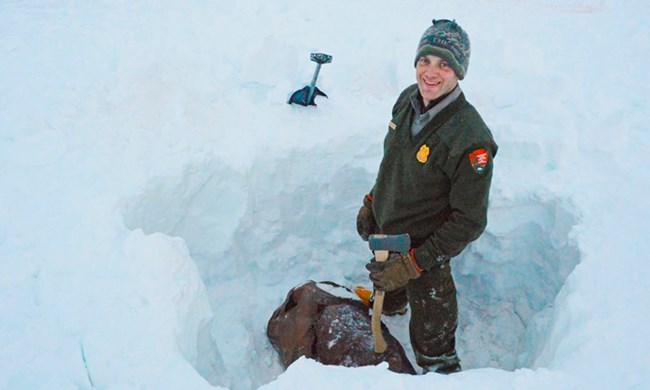 Gates of the Arctic Ranger stands smiling in a deep pit dug to extract an old barrel from the wilderness