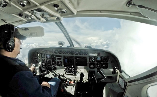 The inside of an airplane cockpit, looking out at the clouds