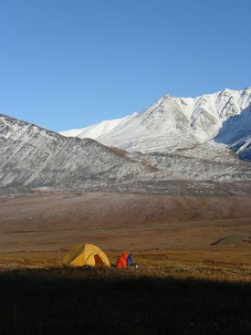 Image of two wilderness travelers sitting on the tundra outside their tent.