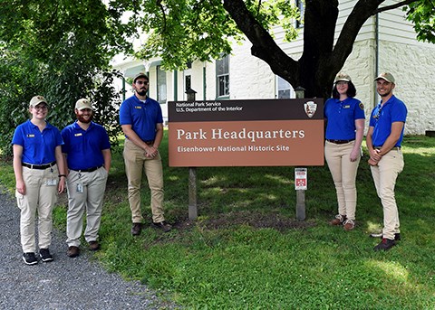 A group of five interns stand next to the Eisenhower National Historic Site Park Headquarter sign.