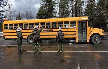 Three rangers wave as a school bus pulls into a parking lot