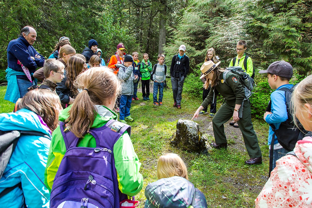 Ranger pointing at large rock is encircled by students wearing backpacks