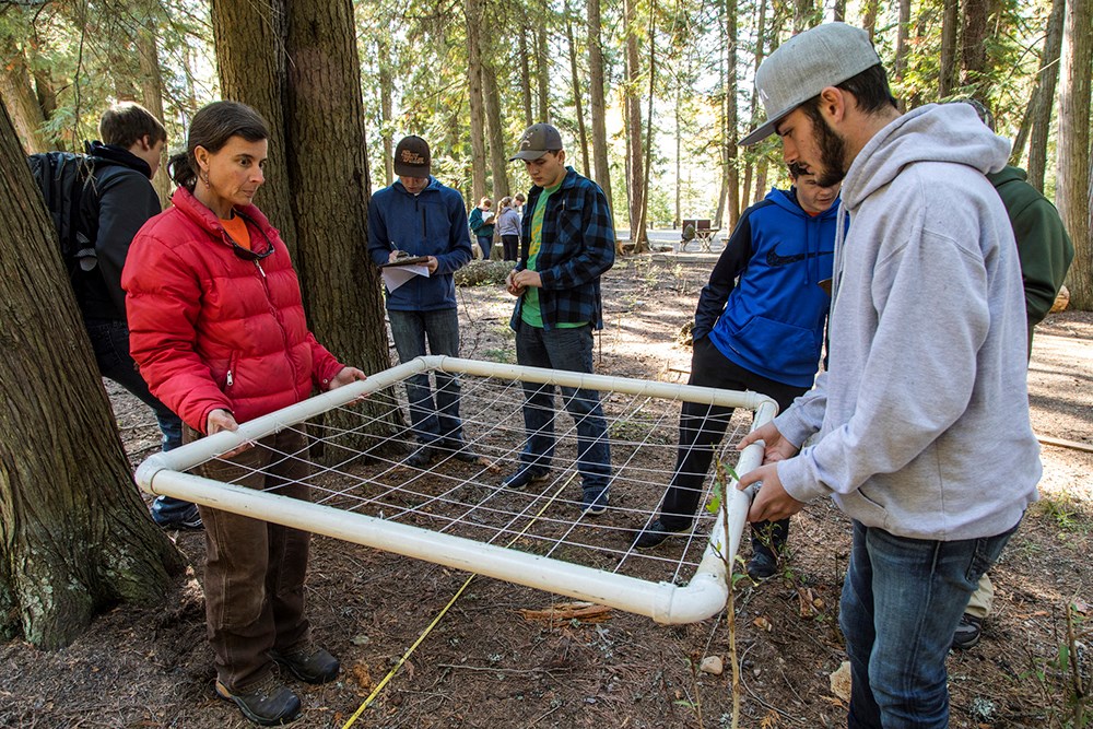 Student and staff member hold a grid plot while other high schoolers observe and/or record data