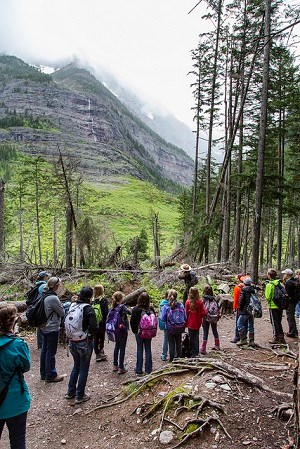 School group on trail faces ranger as she points up a mountainside