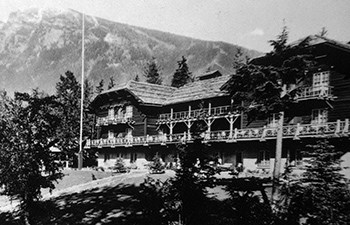 historic image of multistory hotel on grassy hill with mountain in background