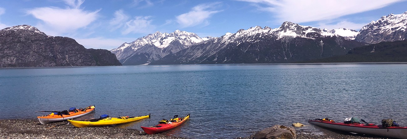 four kayaks sit on a beach in the west arm of Glacier Bay, with water and mountains in the background
