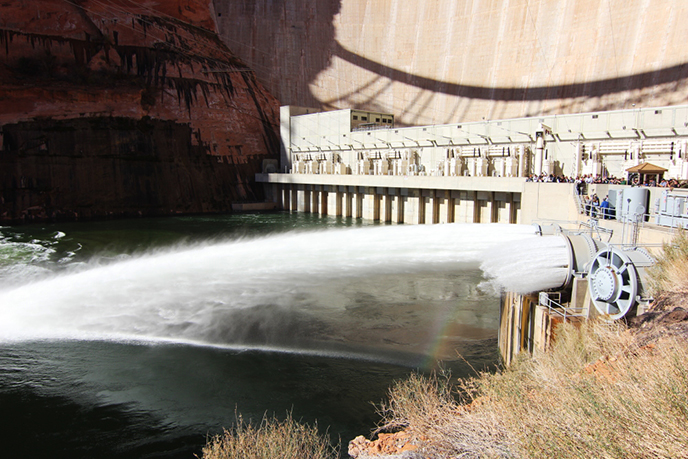 Water gushes from metal tubes at the base of Glen Canyon Dam. A crowd watches.