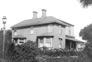 historic image of wood-frame house with gambrel roof, two chimney and bay windows