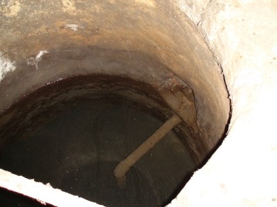 A view of the inside of the well-like structure in the chamber.  The ceramic pipe opening is the large hole just above where the metal pipe goes into the wall of the well in the center of the image.  The water level bisects the ceramic pipe opening.