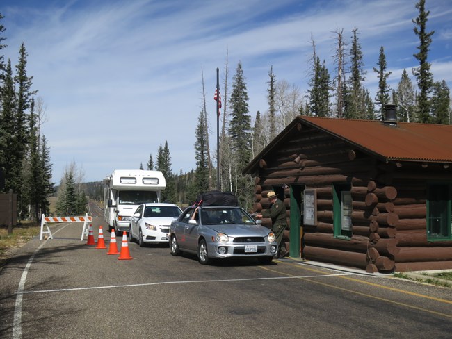 A park ranger hands a map to a person in a vehicle at an entrance station.