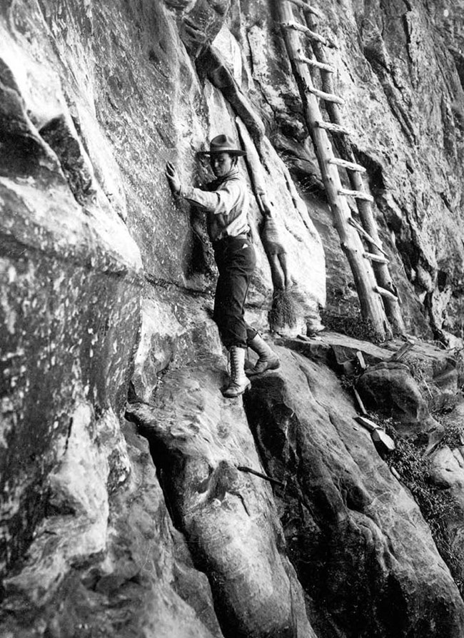 Kolb traversing a vertical cliff face with a ladder close by