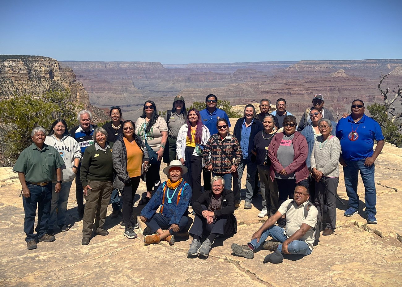 A group of approximately 15 individuals stand at the rim of the canyon for a posed photo.