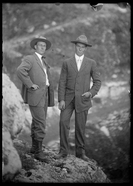 Kolb brothers dressed in coats and hats, standing on a rock in front of Grand Canyon.