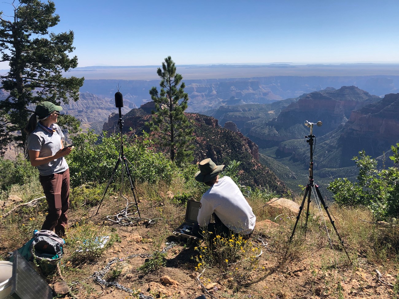 From the edge of a large canyon, two soundscape interns are monitoring noise levels with instruments on tripods.