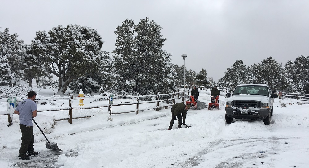 Maintenance workers clearing snow from parking area.