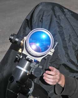 Solar observer under black cloth looking through telescope