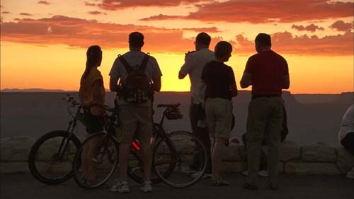 Two bicyclists along with several other people in silhouette are watching sunset at Grand Canyon