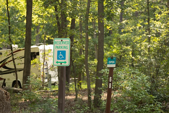 An accessible parking sign and campsite number sign stand in front of a campsite.