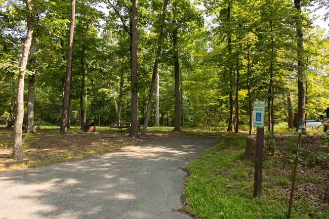 A parking pad leads to a campsite. An accessible reserved parking sign indicates the sites as accessible for parking.