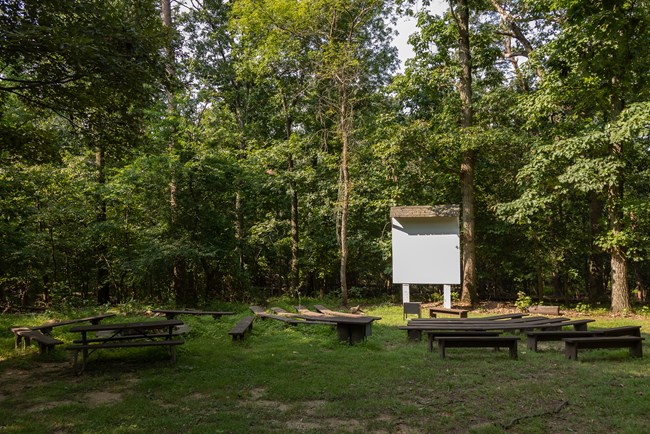 A white, square wood board stands on two legs in the background. Positioned towards the mock movie screen are benches